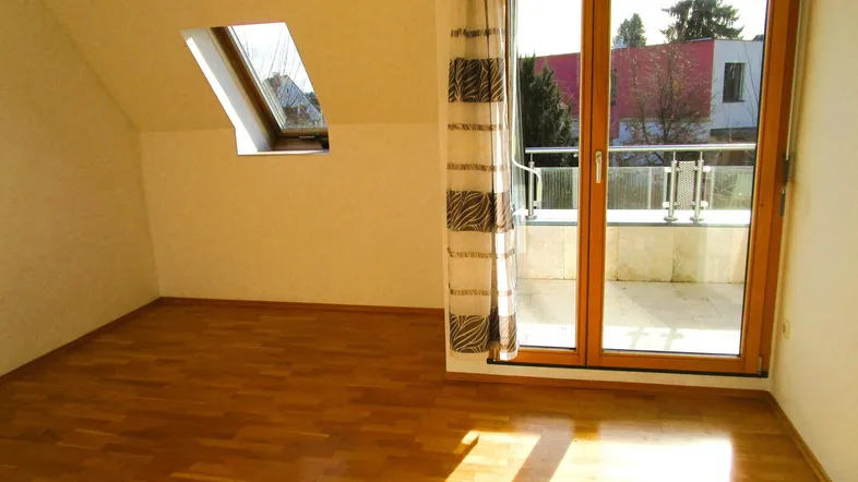 Helles Zimmer im Dachgeschoss mit Holzboden, Dachfenster und Zugang zu einem Balkon.