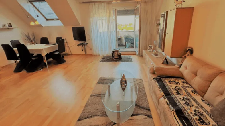 Heller Wohn- und Essbereich mit Holzboden, Dachfenstern und Zugang zu einem Balkon.