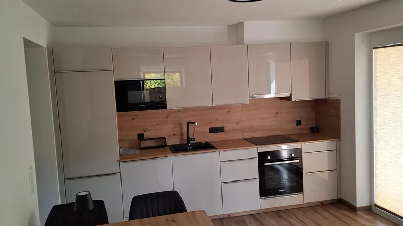 Moderne Küche mit hellen Hochglanzfronten, Holzakzenten und integrierten Geräten, ideal für offenes Wohnen.