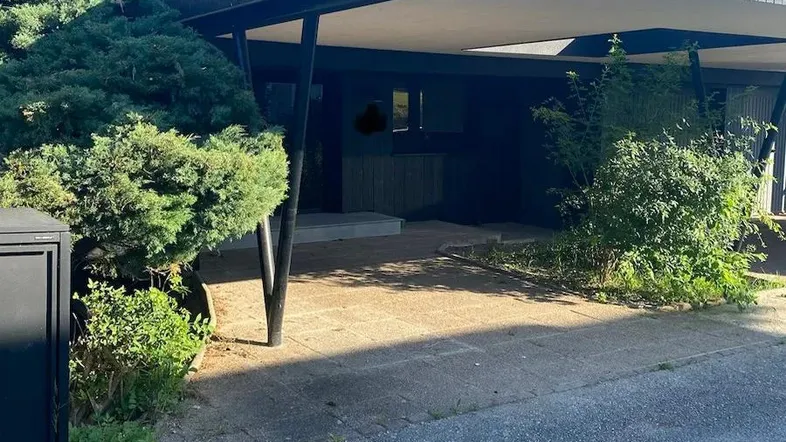 Moderner Eingangsbereich mit überdachtem Carport und grüner Bepflanzung vor dem Haus.