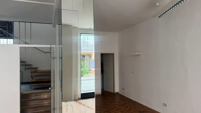 Heller Gewerberaum mit gefliestem Boden, Spiegelflächen und einer Treppe zum Obergeschoss.