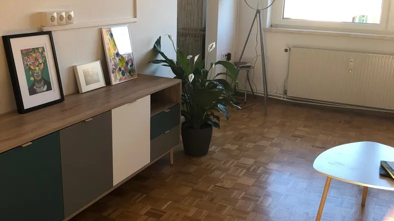 Helles Wohnzimmer mit Parkettboden, modernem Sideboard und großem Fenster.