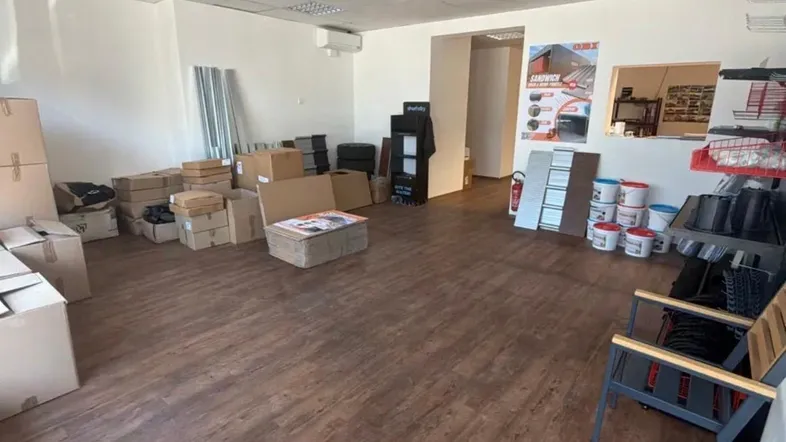 Großer, offener Raum mit Laminatboden, weißen Wänden und abgehängter Decke, teilweise mit Kartons und Auslagen.