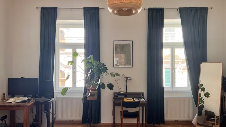 Helles Wohnzimmer mit Fischgrätparkett, zwei großen Fenstern und einem Arbeitsbereich.