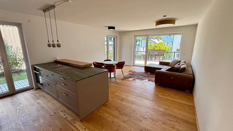 Heller offener Wohn-Essbereich mit moderner Küche, Holzboden und Zugang zum Balkon.