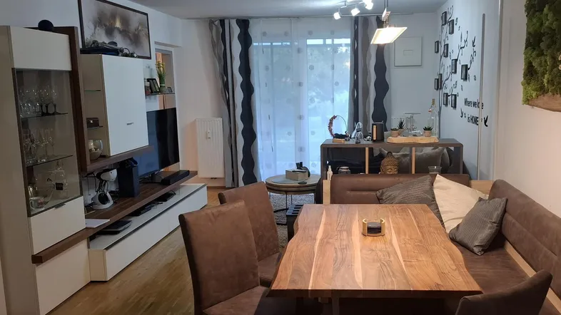 Gemütlicher offener Wohn- und Essbereich mit Holztisch und Zugang zum Balkon.