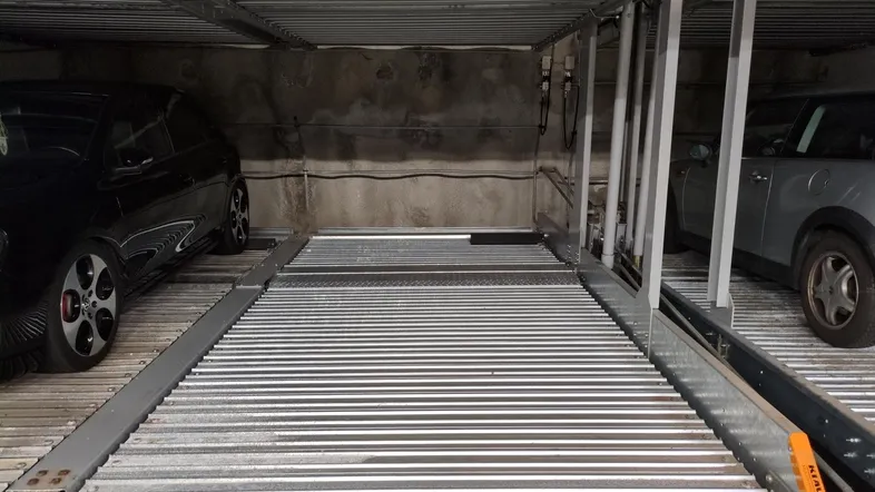 Mehrstöckiges Parksystem in einer Tiefgarage mit zwei geparkten Fahrzeugen und mechanischen Plattformen.