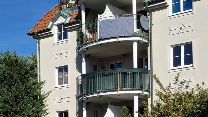 Mehrstöckiges Gebäude mit mehreren Balkonen und traditionellem Mansarddach unter blauem Himmel.