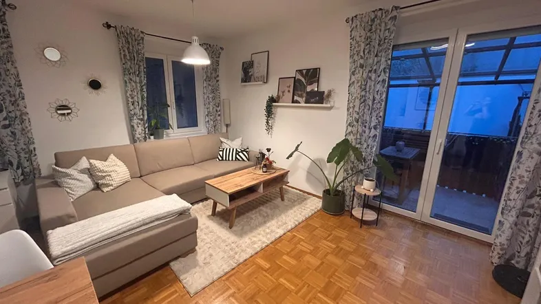 Gemütlicher Wohn- und Essbereich mit Ecksofa, Parkettboden und Zugang zum Balkon.