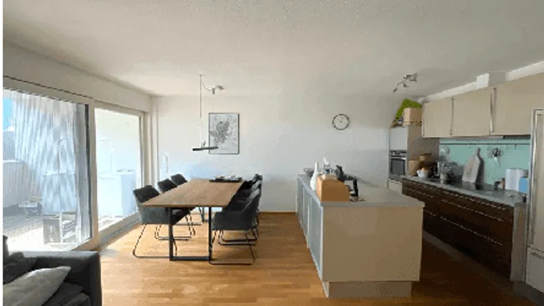 Heller offener Wohn-Essbereich mit moderner Küche, Holzboden und Zugang zum Balkon.