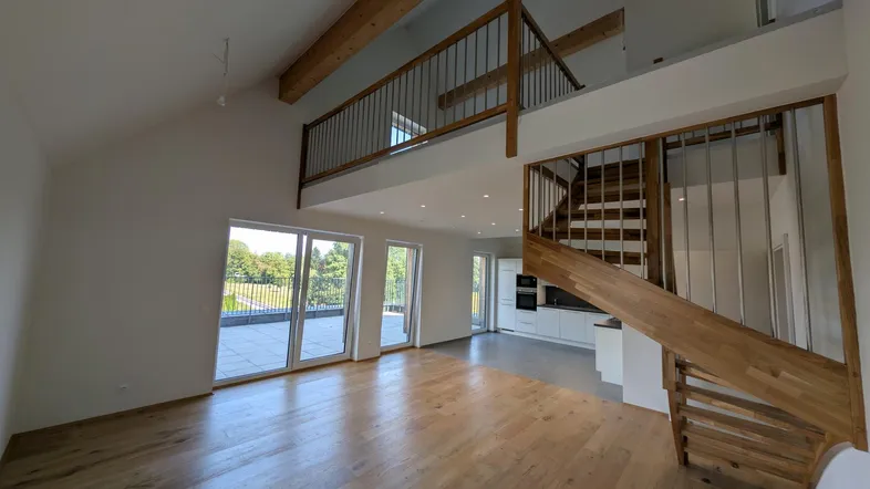 Geräumiger offener Wohnbereich mit Holzboden, hohen Decken, sichtbaren Balken und Zugang zur Terrasse.