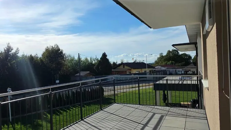 Sonniger Balkon mit grauen Fliesen und Metallgeländer, bietet einen weiten Blick ins Grüne.