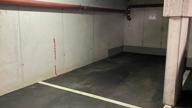 Tiefgaragenstellplatz mit robusten Betonwänden, Asphaltboden und sichtbaren Installationen an der Decke.