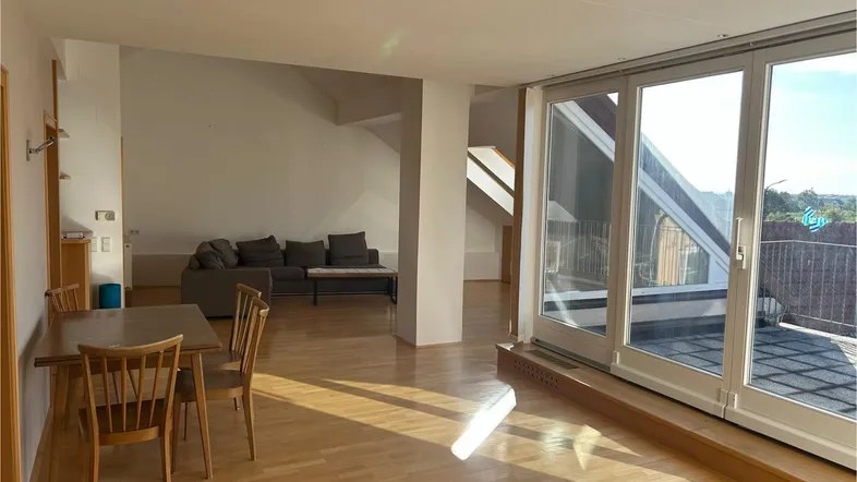 Helles Wohn- und Esszimmer mit Holzboden, großen Fenstern und Zugang zu einer Terrasse.