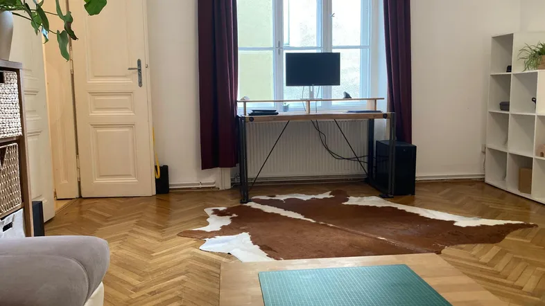 Helles Wohnzimmer mit Schreibtisch, großem Fenster und Fischgrätparkettboden.
