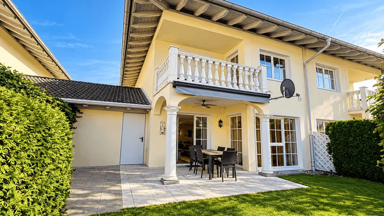 Hinteransicht des Hauses mit großer Terrasse, Gartenmöbeln und gepflegtem Rasen.