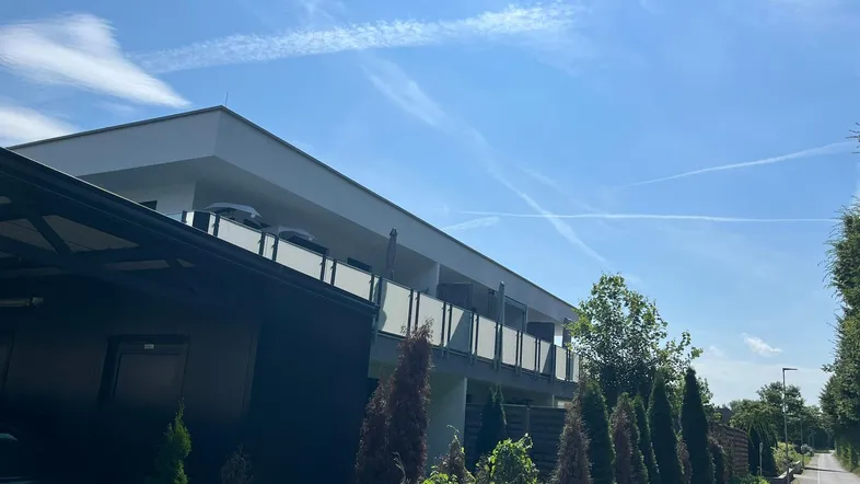 Modernes Mehrfamilienhaus mit weißer Fassade, Balkonen und einem Carport unter blauem Himmel.