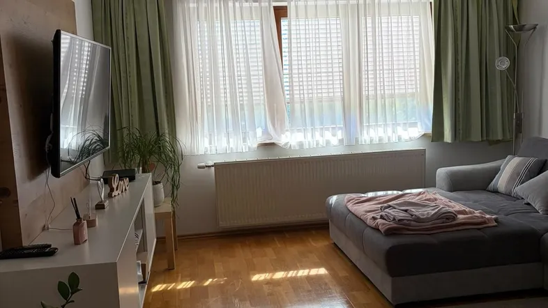 Helles Wohnzimmer mit Holzfußboden, bequemer Couch und großem Fenster mit Vorhängen.