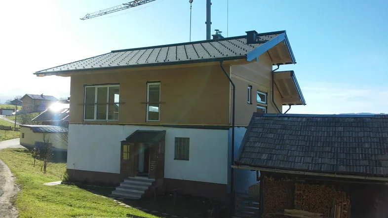 Neues Einfamilienhaus mit Satteldach und Holzfassade im Bau, umgeben von grüner Landschaft.
