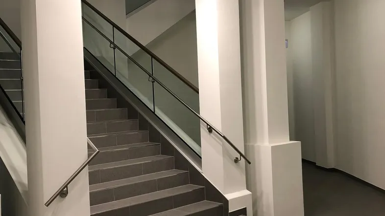 Treppenhaus mit modernem Geländer, grauen Fliesen und stilvoller Deckenleuchte.