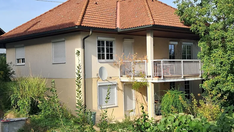 Ansicht des Hauses von außen mit Ziegeldach, beiger Fassade und einem Balkon.