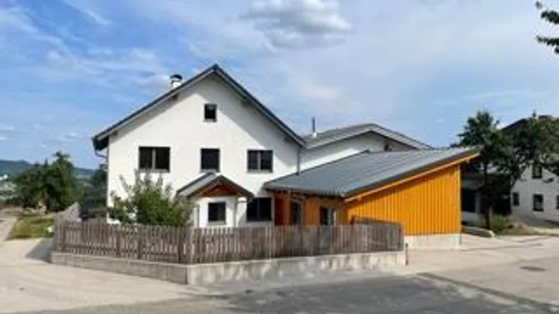 Weißes Wohnhaus mit Satteldach und einem modernen Anbau mit orangefarbener Holzfassade.
