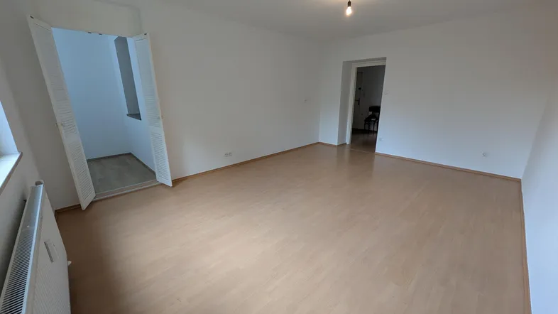 Helles, leeres Zimmer mit Laminatboden und Heizkörper, bereit zur individuellen Gestaltung.