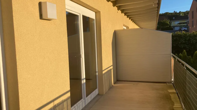 Sonniger Balkon mit gelber Fassade und Blick ins Grüne, ideal für entspannte Stunden.
