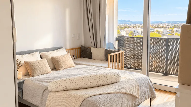 Helles Schlafzimmer mit Holzboden, gemütlichem Bett und Zugang zu einem Balkon mit Stadtblick.