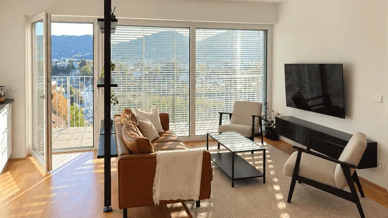 Helles Wohnzimmer mit Holzboden, moderner Einrichtung und Zugang zu einem Balkon mit Weitblick.