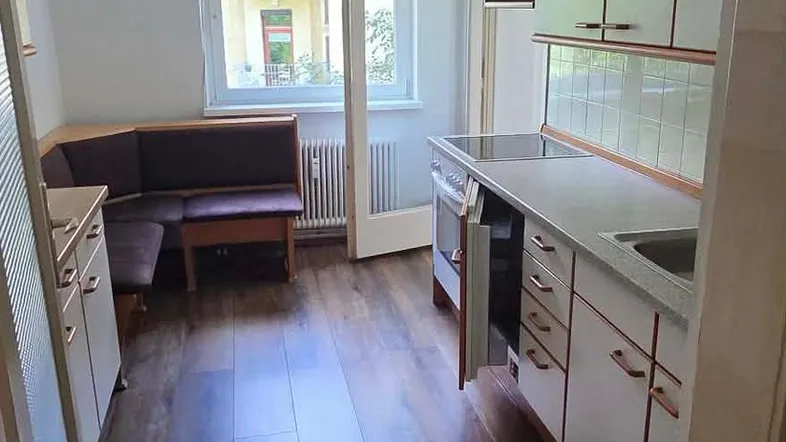 Helle Küche mit Essbereich, Einbauschränken und Blick ins Grüne durch das Fenster.
