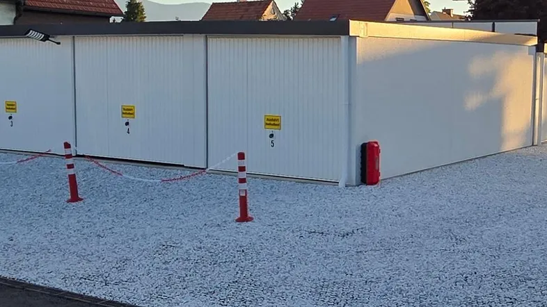 Reihe moderner, weißer Garagenboxen mit flachem Dach und Schotterfläche davor, ideal für Lagerung oder Fahrzeuge.