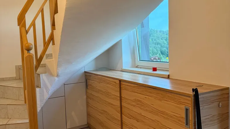 Heller Treppenaufgang mit Holzgeländer, Fliesenboden und praktischem Einbauschrank unter der Schräge.