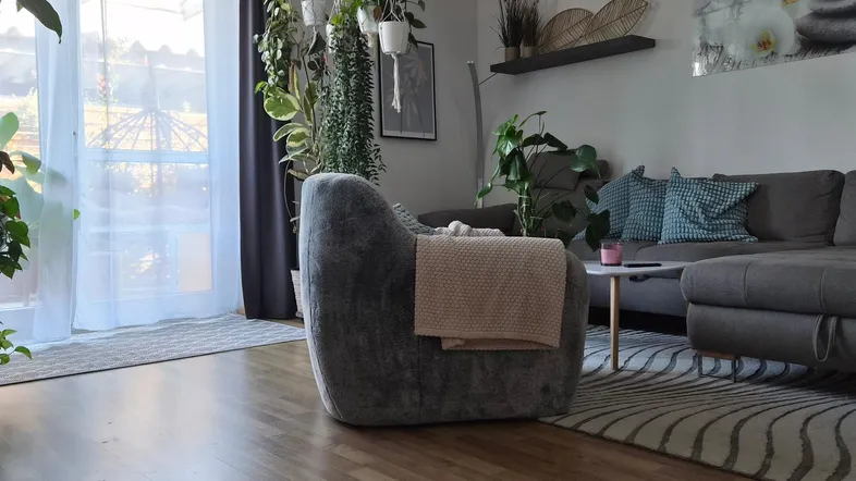 Helles Wohnzimmer mit Holzboden, gemütlicher Sitzecke und vielen Pflanzen, die eine natürliche Atmosphäre schaffen.