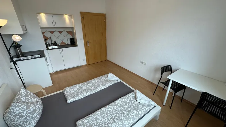 Helles Zimmer mit Bett, Esstisch und integrierter Küchenzeile, ideal für ein Studio-Apartment.