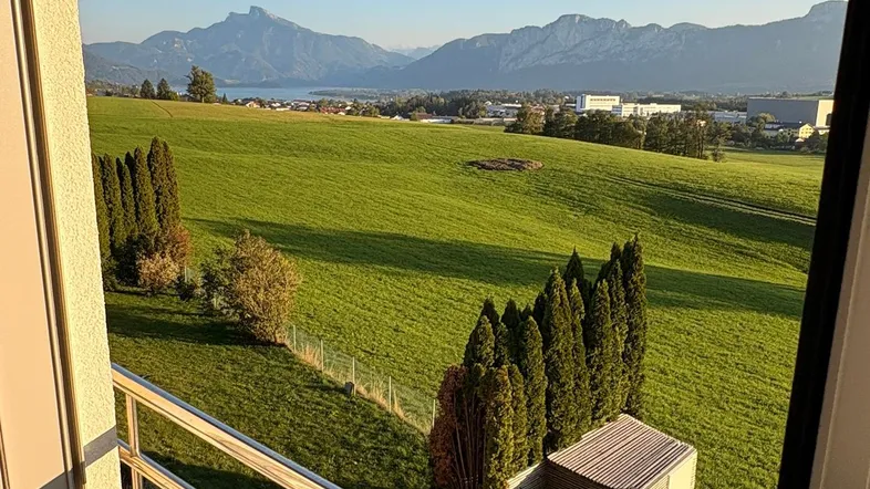 Panoramablick vom Balkon über grüne Felder, einen See und majestätische Berge in der Ferne.