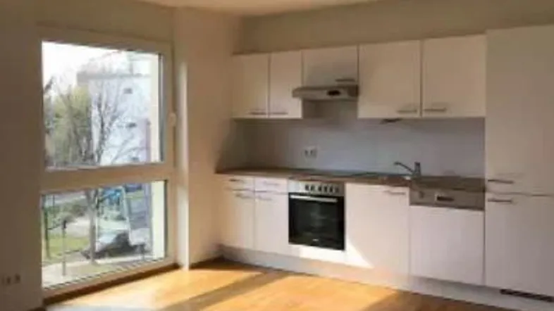 Helle, offene Küche mit weißen Schränken, Holzboden und großem Fenster mit Blick ins Grüne.