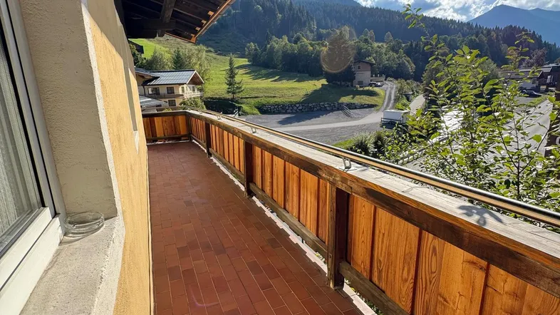 Sonniger Balkon mit traditionellem Holzgeländer und weitem Blick auf die umliegenden Berge.