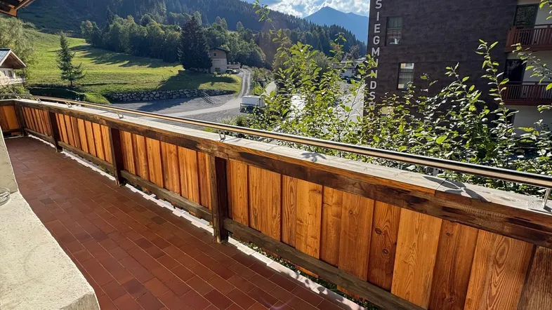 Sonniger Balkon mit Holzgeländer und beeindruckendem Blick auf die umliegenden Berge.