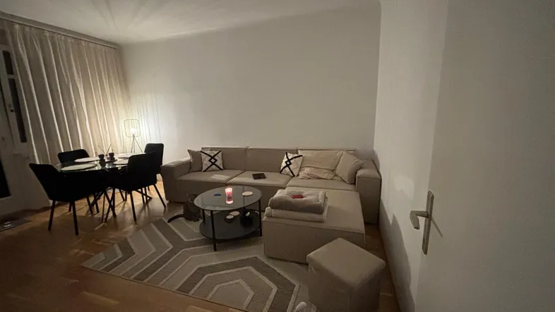 Gemütlicher Wohn- und Essbereich mit beigem Sofa, modernem Teppich und Holzboden.