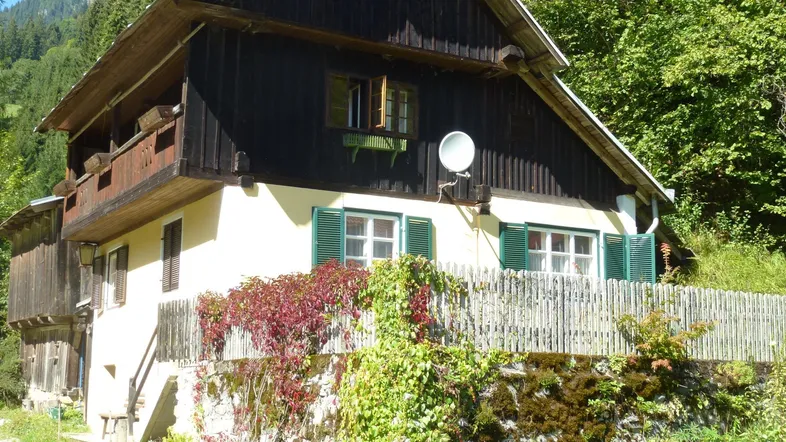Traditionelles Haus mit Holzbalkonen, grünen Fensterläden und umgeben von üppiger Natur.