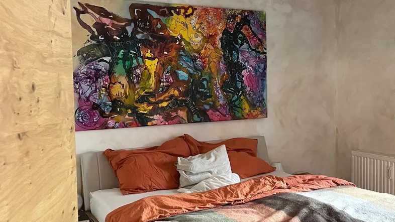 Helles Schlafzimmer mit Holzboden, großem Bett und farbenfrohem Kunstwerk an der Wand.