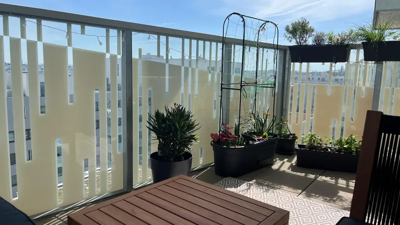 Heller Balkon mit Holztisch, Pflanzen und Blick auf die Stadt.