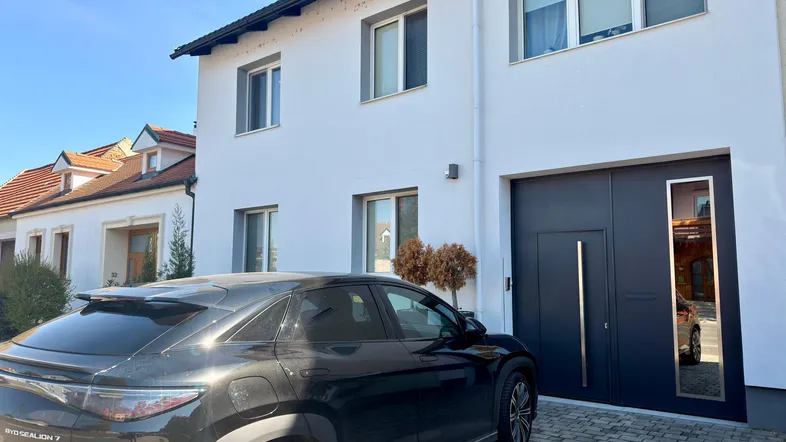 Moderne Hausfassade in Weiß mit dunklem Eingangsbereich und gepflasterter Auffahrt.