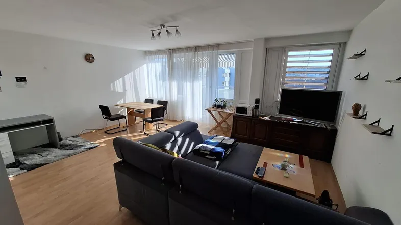 Helles Wohn- und Esszimmer mit Parkettboden, großem Sofa und Zugang zum Balkon.