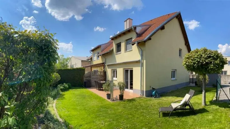 Großzügiger Gartenbereich hinter dem Haus mit Rasenfläche, Bäumen und einer Sonnenliege.