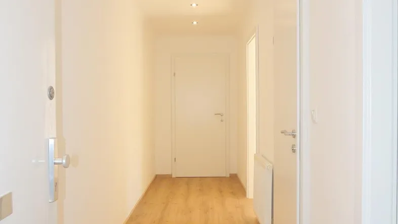 Heller Flur mit modernem Laminatboden und Einbaustrahlern, der zu weiteren Räumen führt.