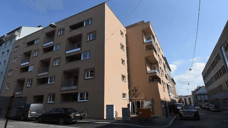 Modernes Mehrfamilienhaus mit mehreren Balkonen und schlichter Fassadengestaltung an einer Stadtstraße.