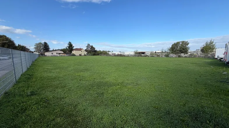 Weitläufiges grünes Grundstück mit Blick auf umliegende Gebäude und einen blauen Himmel.