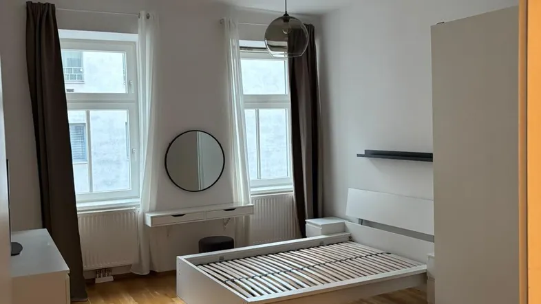 Helles Schlafzimmer mit Holzboden, einem Bettgestell und einem weißen Kleiderschrank.